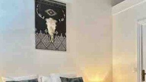 A bedroom with a bed, pillows, a colorful blanket, a wall art piece, and a nightstand with a lamp.