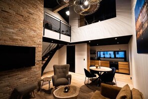 A spacious living area with a brick wall, a staircase, a dining area, and a kitchen. - Broncks Apartments (Tórshavn)