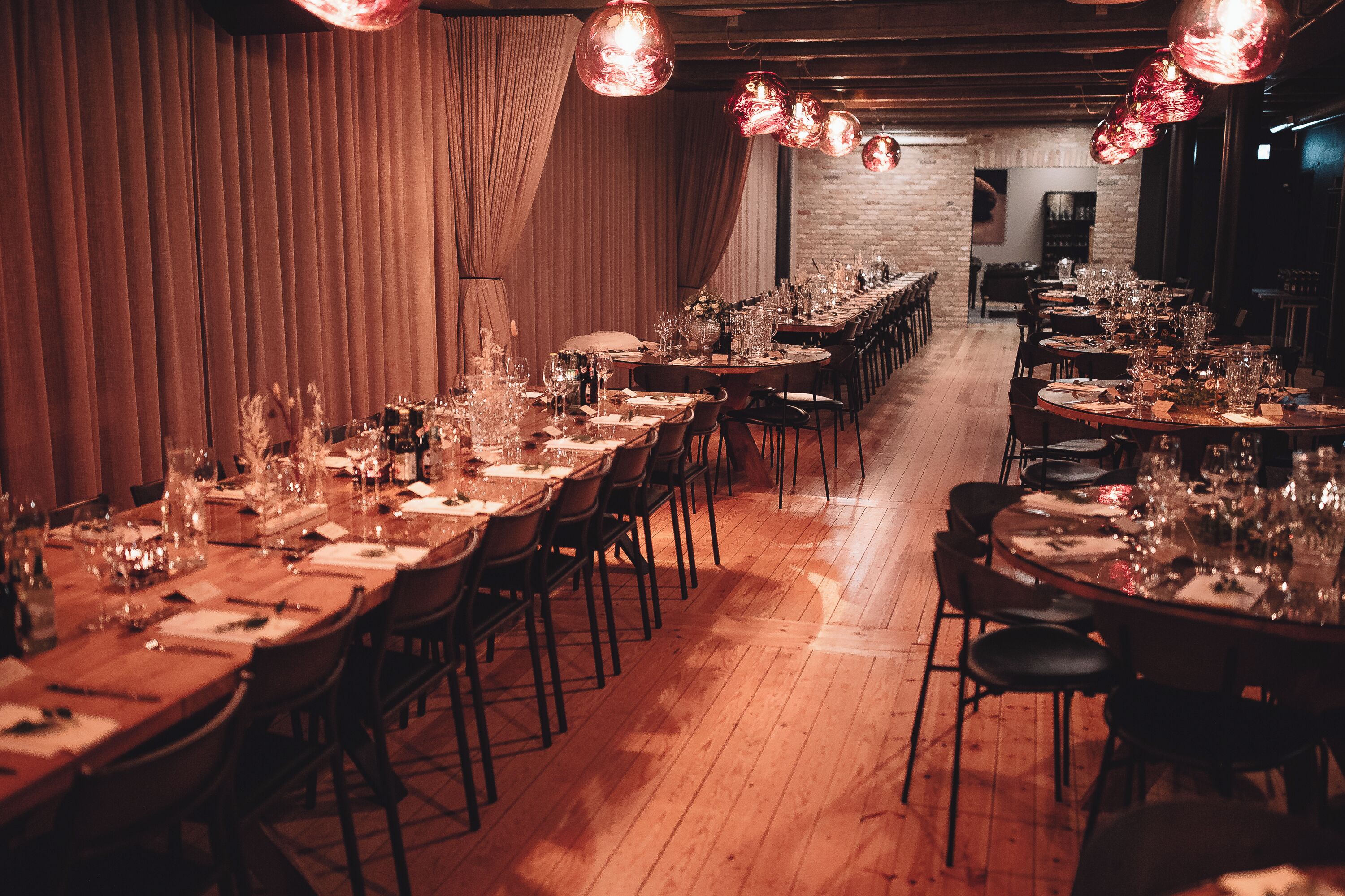 A long dining table set with multiple chairs, surrounded by wooden flooring and draped curtains.