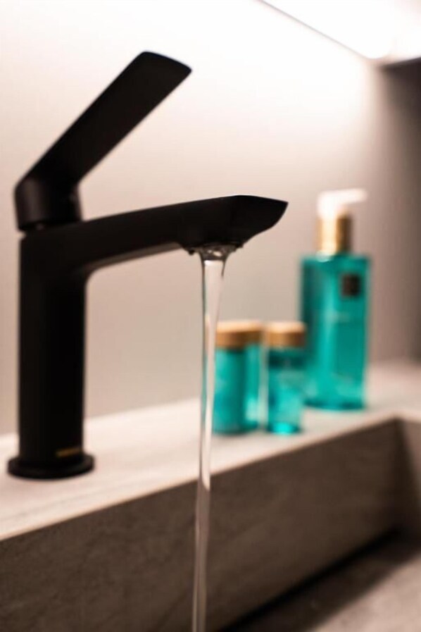 A modern bathroom with a black faucet and a visible water stream. - Broncks Apartments (Tórshavn)