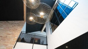 Ένας μοντέρνος εσωτερικός χώρος με μια ξεχωριστή γεωμετρική διαμόρφωση στην οροφή, έναν τοίχο από τούβλα και μια γυάλινη πρόσοψη.