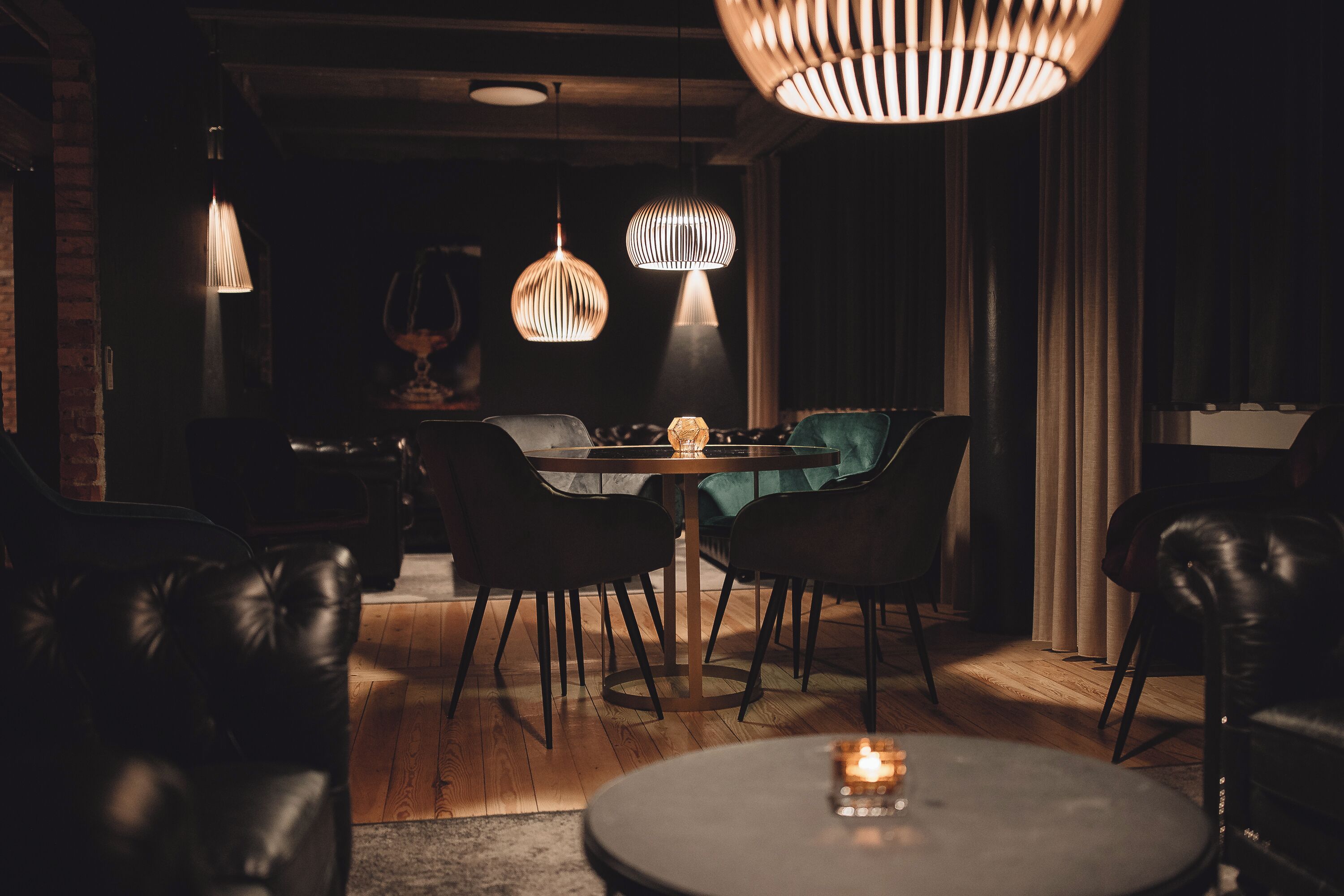 Un comedor tenuemente iluminado con una mesa redonda, sillas de cuero negro e iluminación colgante.