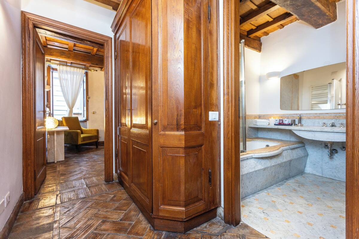 A wooden hallway leading to a bathroom with a marble floor and a large mirror.