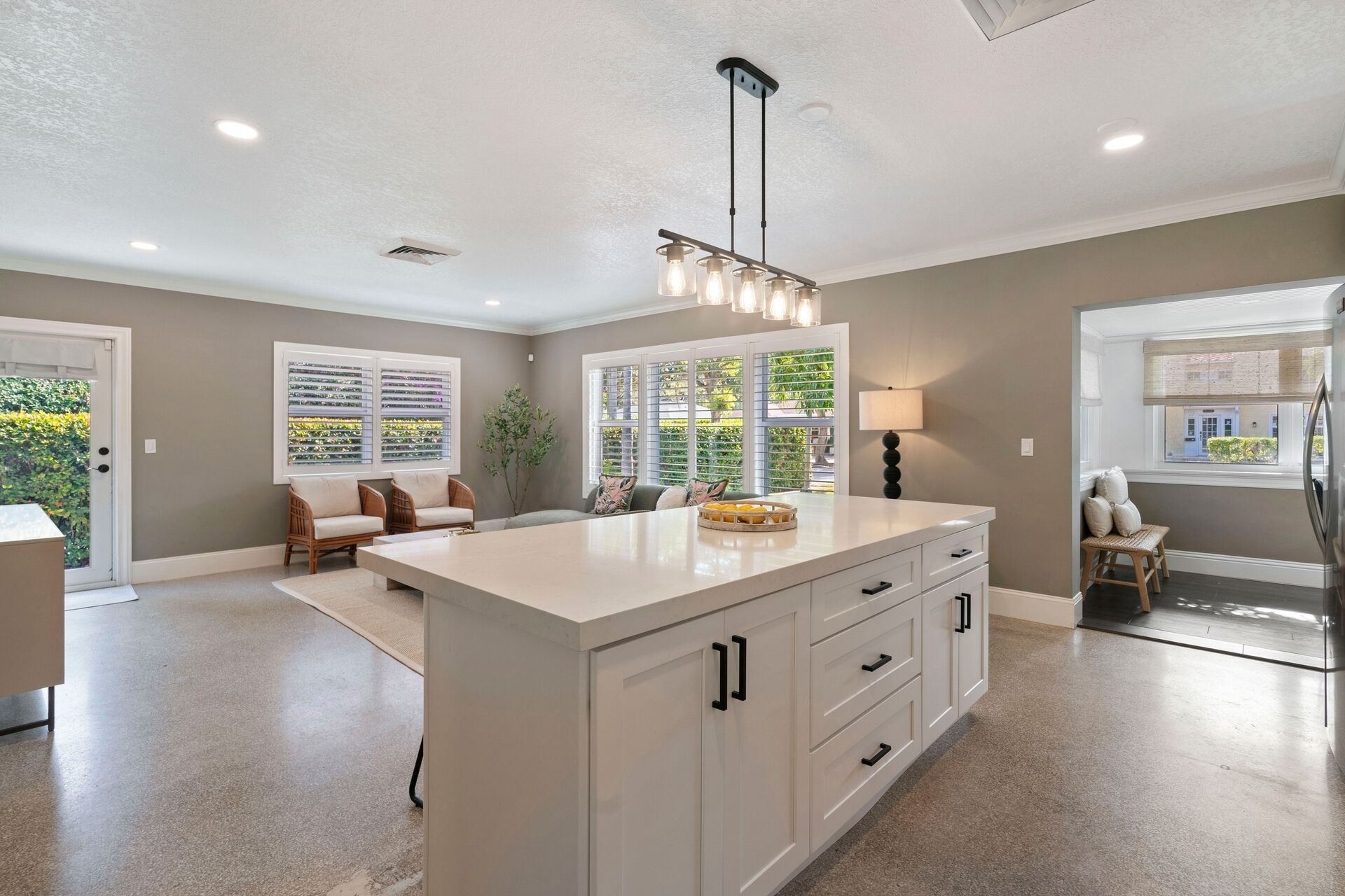 A spacious kitchen with a large island, recessed lighting, and a view of the outdoors through the windows.