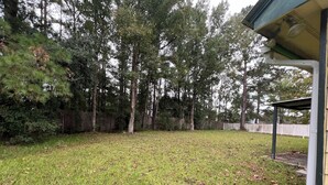A backyard with a wooden fence, a covered patio area, and a variety of trees. - Sleeps 10•Near HWY I-95,40,17 & Kings Bay navybase,Cumberland Island,JAX airport (Kingsland)