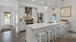 Une cuisine moderne avec des meubles blancs, des appareils en acier inoxydable et un grand îlot central doté de tabourets de bar.