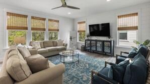 Un salon spacieux avec un canapé beige, un tapis bleu à motifs, une table basse ronde et un meuble en bois foncé sur lequel est fixé un téléviseur.