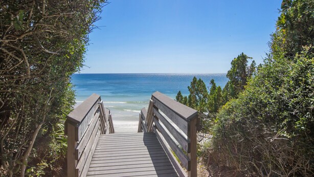Une promenade en bois qui mène à une plage où l’eau est d’un bleu cristallin et qui offre une vue sur l’océan.
