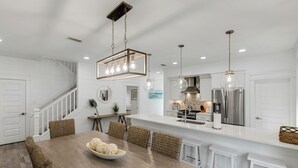 Une cuisine spacieuse dotée d’un îlot central, d’appareils électroménagers en acier inoxydable et de luminaires suspendus.