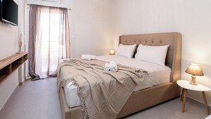 A neatly arranged bedroom with a bed, bedside lamps, a TV, and a window with curtains. - Niman Beachside Apartments (Chania)