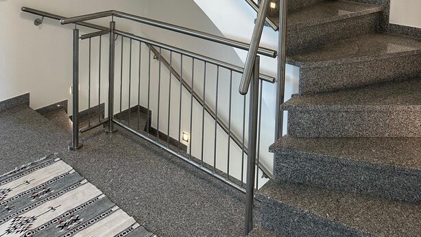 Una moderna scala con ringhiere in metallo e gradini in granito, che conduce a un pianerottolo con un lampadario.