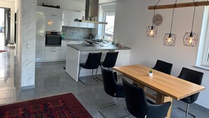 Una cucina moderna con mobili bianchi, un'isola centrale e sedie nere attorno a un tavolo di legno.