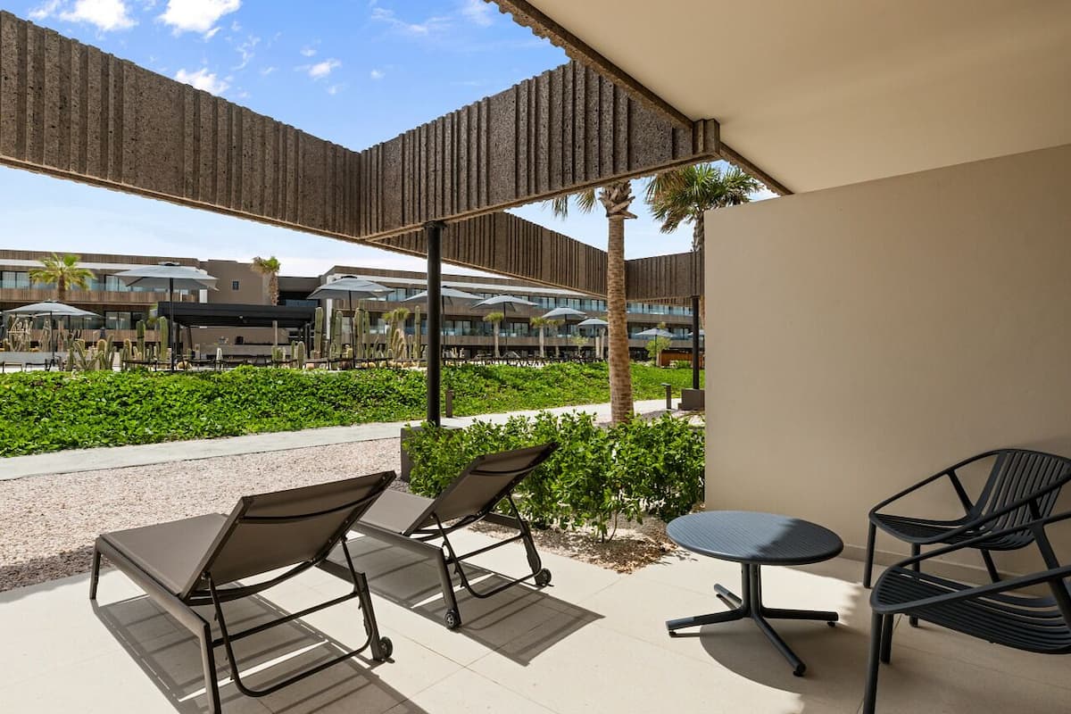 An outdoor seating area with two lounge chairs and a small table, surrounded by a low wall and palm trees.