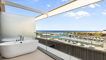 A modern bathroom with a freestanding bathtub, a large window overlooking a pool and beach area.