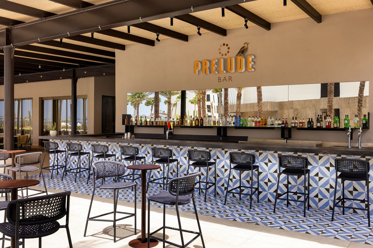An outdoor bar area with a tiled floor, multiple seating arrangements, and a bar counter stocked with various bottles.