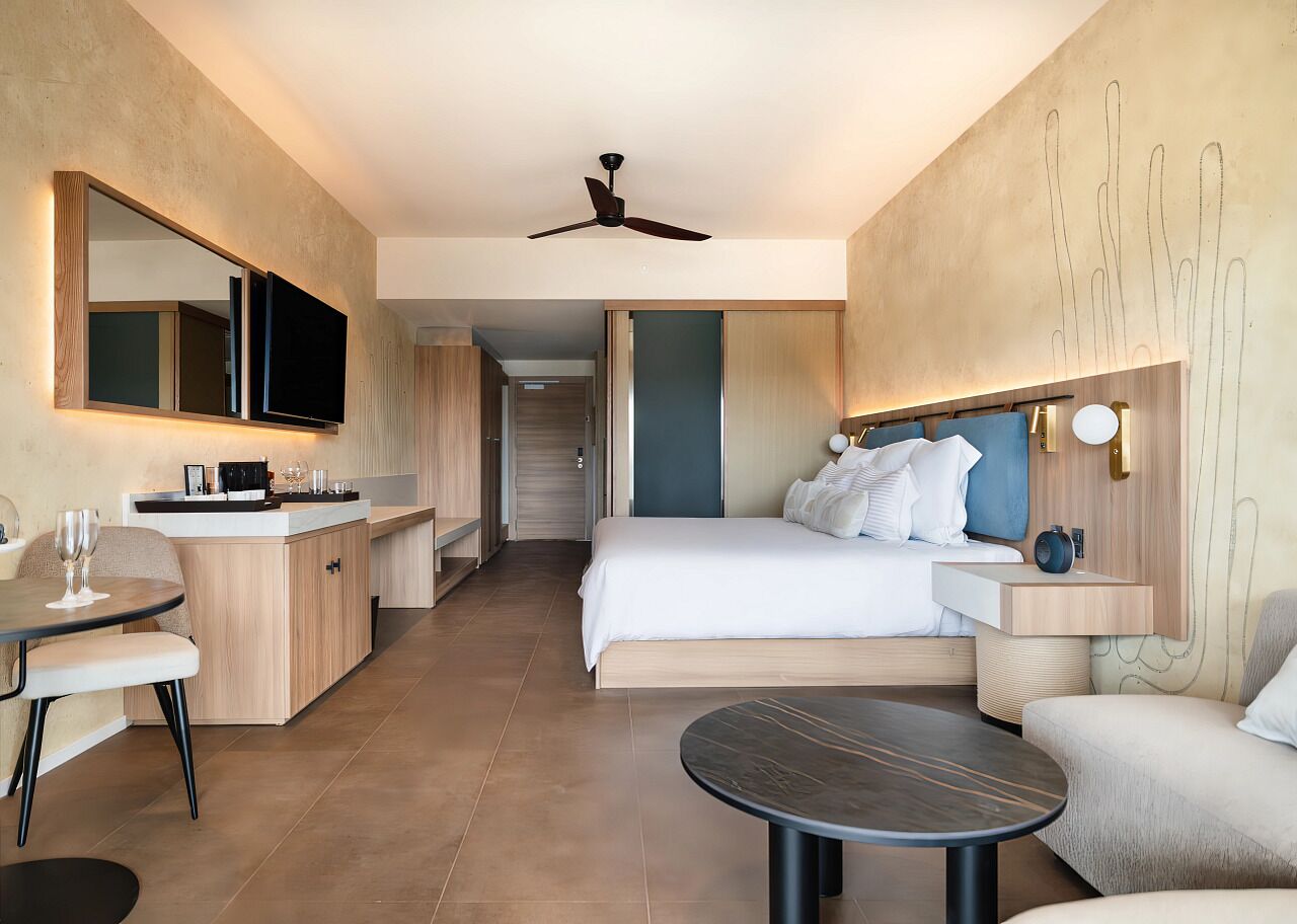 A modern hotel room with a bed, a desk, a chair, a round table, and a ceiling fan.