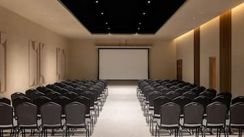A conference room with rows of chairs facing a large screen, a wooden accent wall, and a ceiling with recessed lighting.