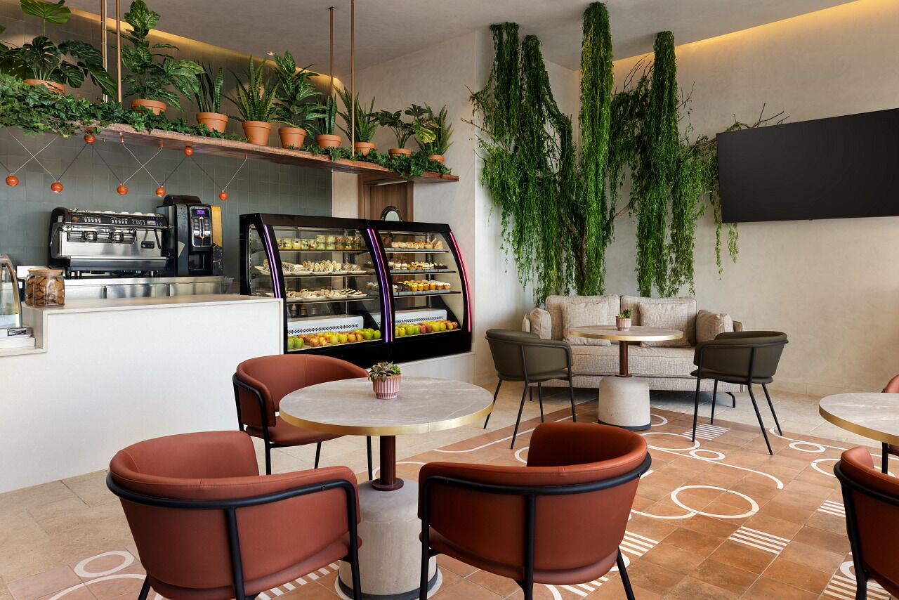 Una cafetería moderna con una máquina de café, una vitrina de postres y varias mesas y sillas.