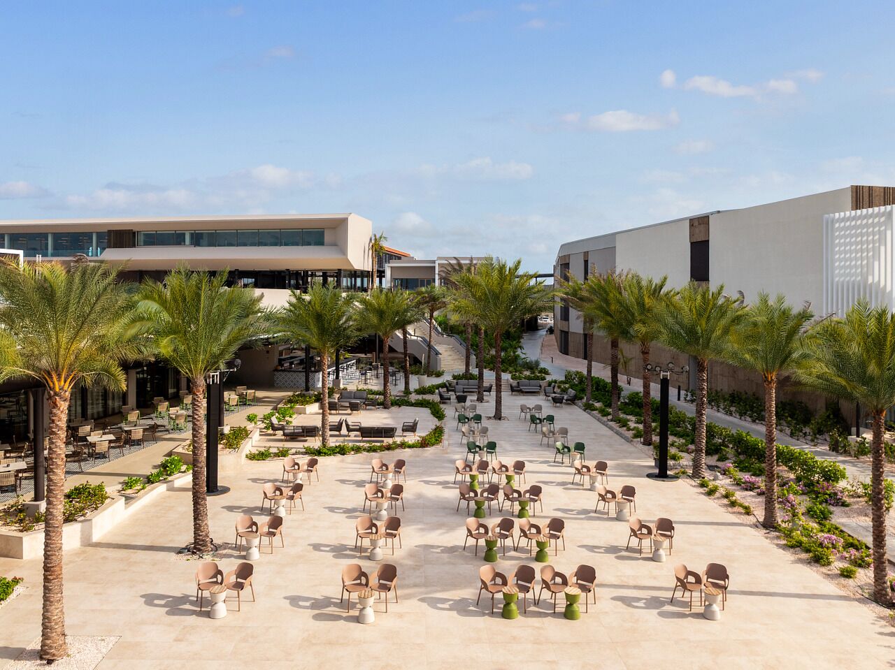 A spacious outdoor area with multiple seating arrangements, palm trees, and a modern building in the background.
