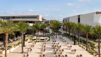 Un amplio espacio al aire libre con diversas opciones de asientos, palmeras y un edificio moderno de fondo.