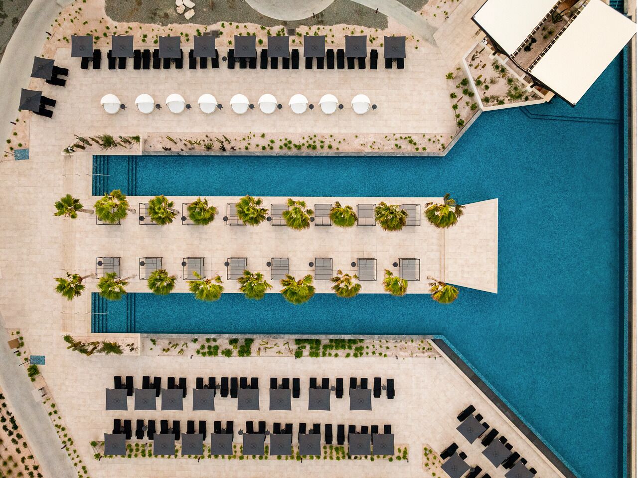 Vista aérea de un resort con piscina central, múltiples tumbonas y zonas con sombra.