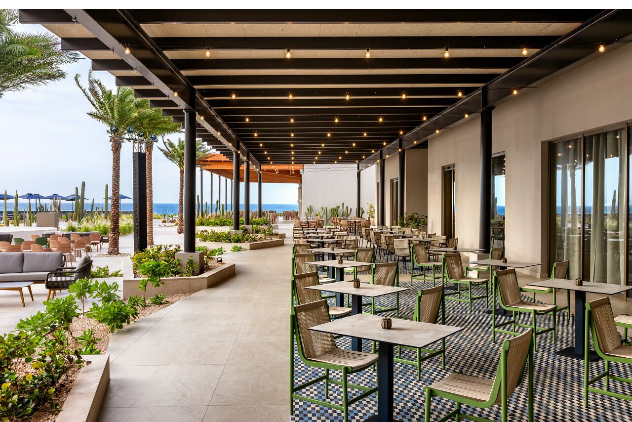 An outdoor patio area with tables and chairs, a view of the ocean, and a covered walkway.