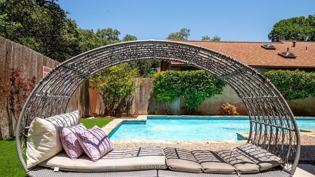 Un fauteuil suspendu circulaire en osier, doté de coussins et offrant une vue sur une piscine.