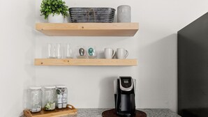 Un comptoir de cuisine avec une machine à café, des bocaux et de la verrerie, le tout posé sur des étagères en bois.