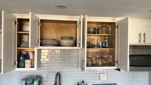 A kitchen with open cabinets displaying dishes, glasses, and a coffee maker. - Oceanfront 1-bedroom condo with Deck Views in Rye (Rye)