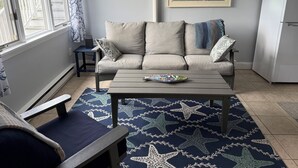 A living room with a sofa, a coffee table, a chair, a patterned rug, a mirror, and a refrigerator. - Oceanfront 1-bedroom condo with Deck Views in Rye (Rye)