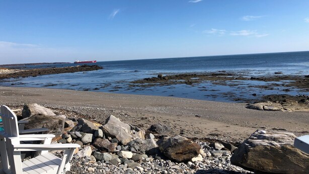 A rocky beach with a chair and a large log. - Oceanfront 1-bedroom condo with Deck Views in Rye (Rye)