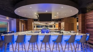 A modern bar area with a central island, bar stools, and a large screen. - Ocean/Pool View 703- Relax and recharge at Fort Myers Beach (Fort Myers Beach)