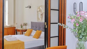 A hotel room with a bed, a desk, a chair, a vase with flowers, and a mirror. - 4bnb - Spacious Gracchi Apartment (Rome)