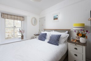 Une chambre à coucher comprenant un lit, une table de chevet, une lampe et une fenêtre donnant sur un mur en pierre.