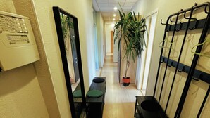 A hallway with a mirror, a potted plant, a bench, and a coat rack. - Artihost (Panevezys)