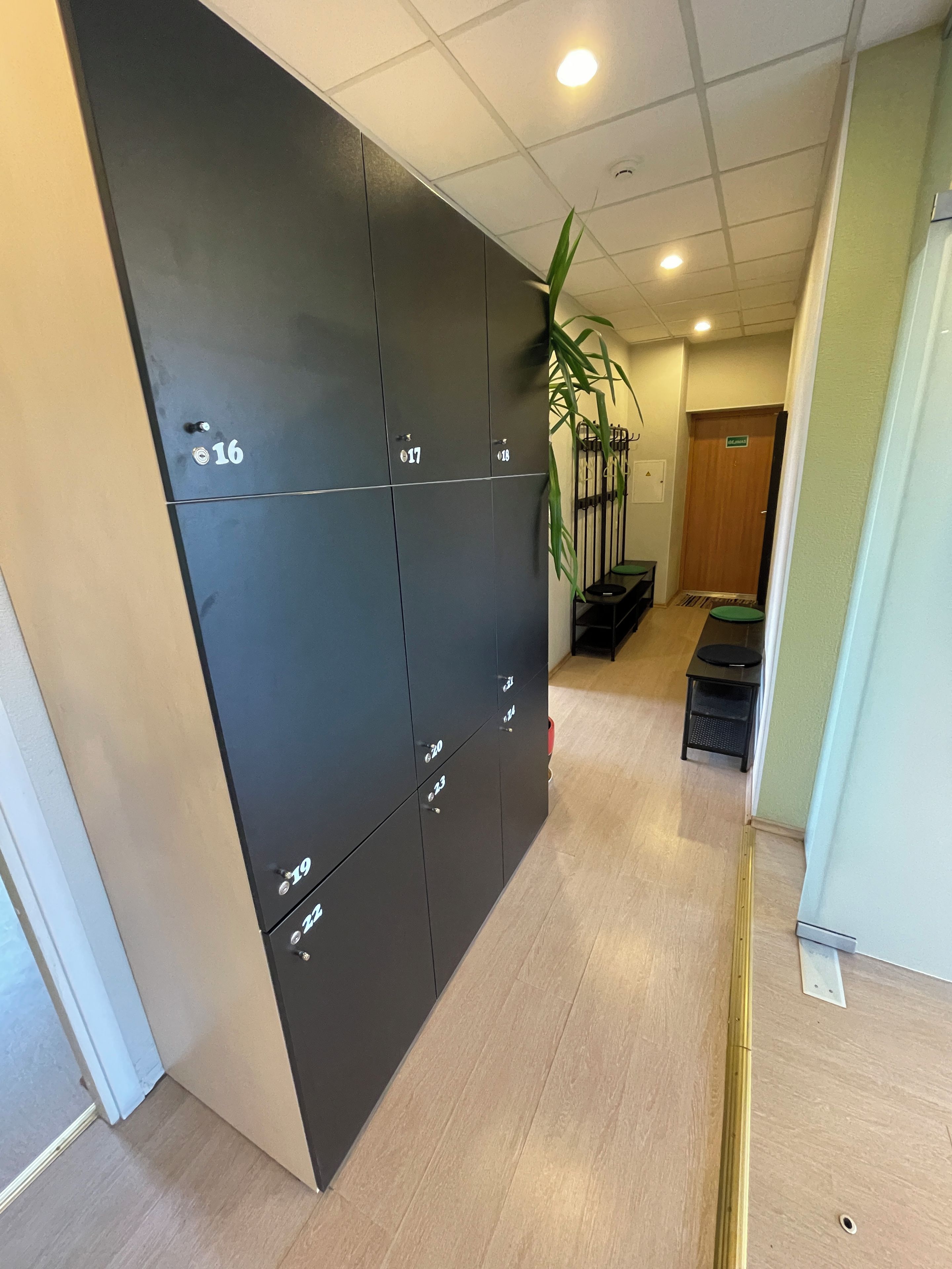 A hallway with lockers numbered 16 to 19, a wooden floor, and a door with a sign.