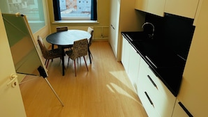 A compact kitchen with a round table and chairs, a black stove, and a window with a view of buildings. - Artihost (Panevezys)