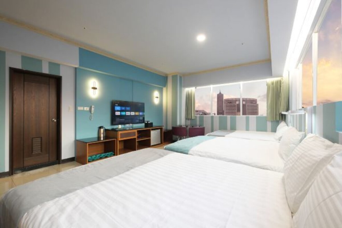 Camera d'albergo con due letti, una televisione, una scrivania e una finestra vista città.