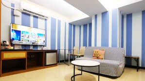 A room with a striped blue and white wall, a sofa with a striped cover, a small round table, a television on a wooden stand, and a small kitchenette area. - IHI loveriver Hotel (Kaohsiung)