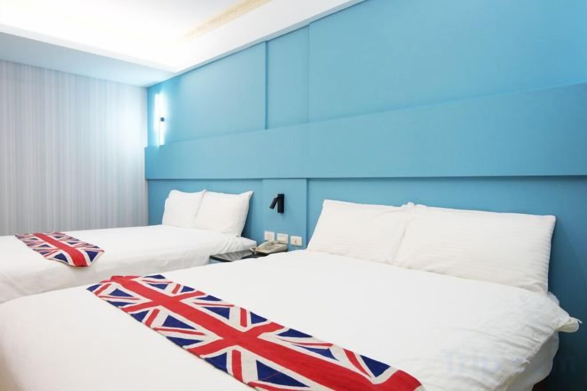 A hotel room with two beds, a blue accent wall, and a white bedspread with a Union Jack design.