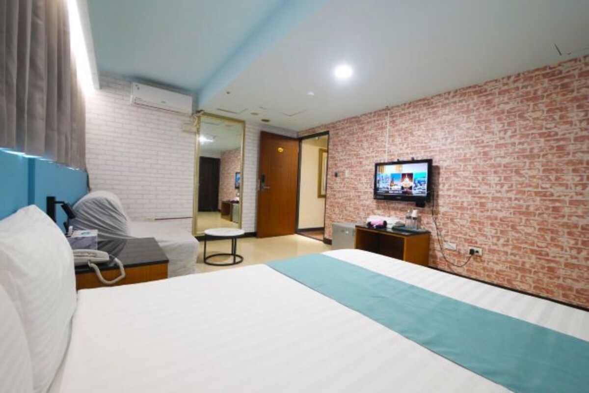 Una camera d'albergo con un letto, una scrivania, una sedia, una televisione e una parete con motivo a mattoni.