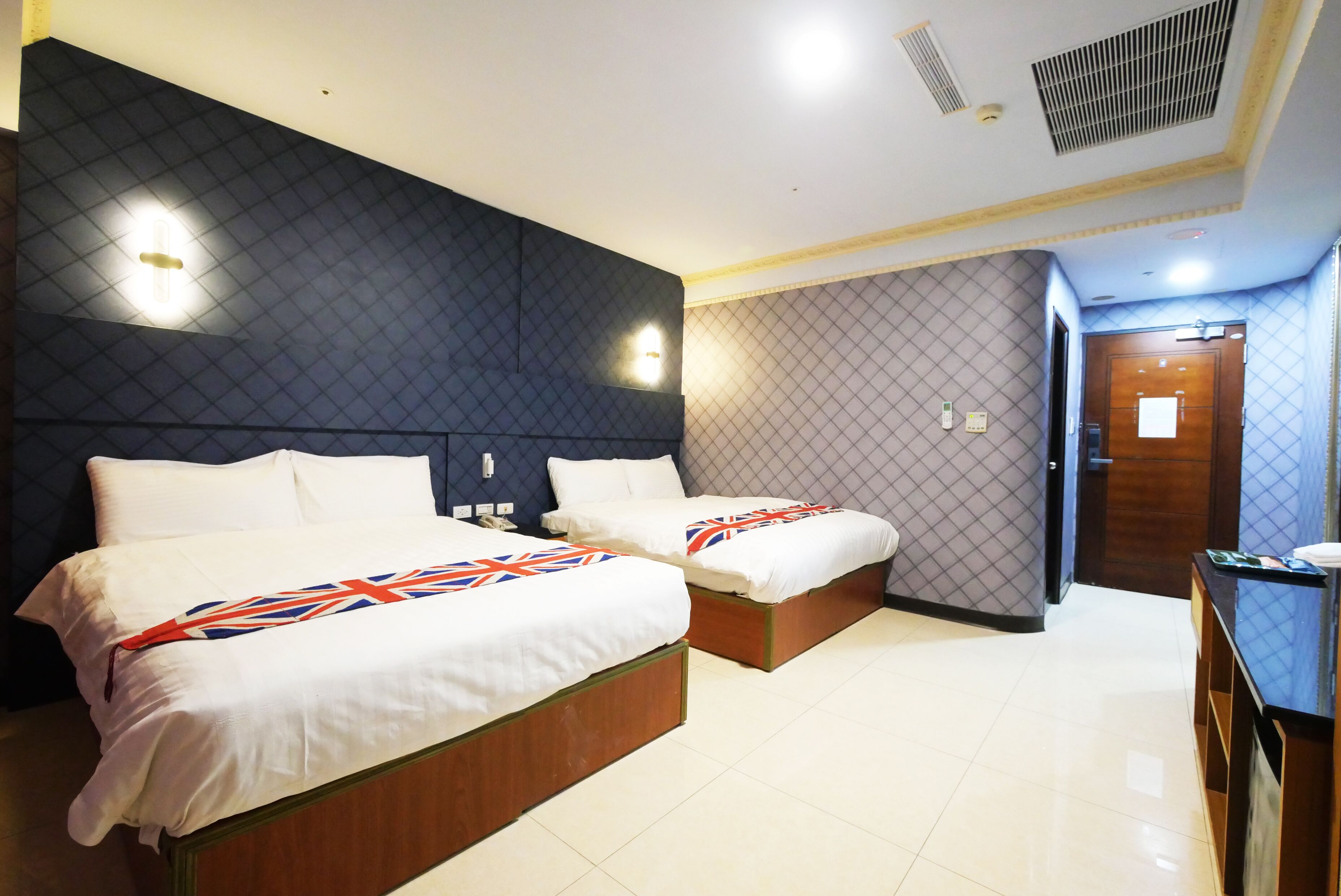 Une chambre d’hôtel avec deux lits, un mur à motifs sombres et une porte en bois.