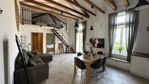 A spacious living area with a wooden staircase, a dining table with chairs, a sofa, and a television mounted on the wall. - Apartment Olivia (Piran)