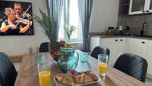 A dining table with breakfast items, including croissants and juice, in a modern kitchen with a TV displaying a violin performance. - Apartment Olivia (Piran)