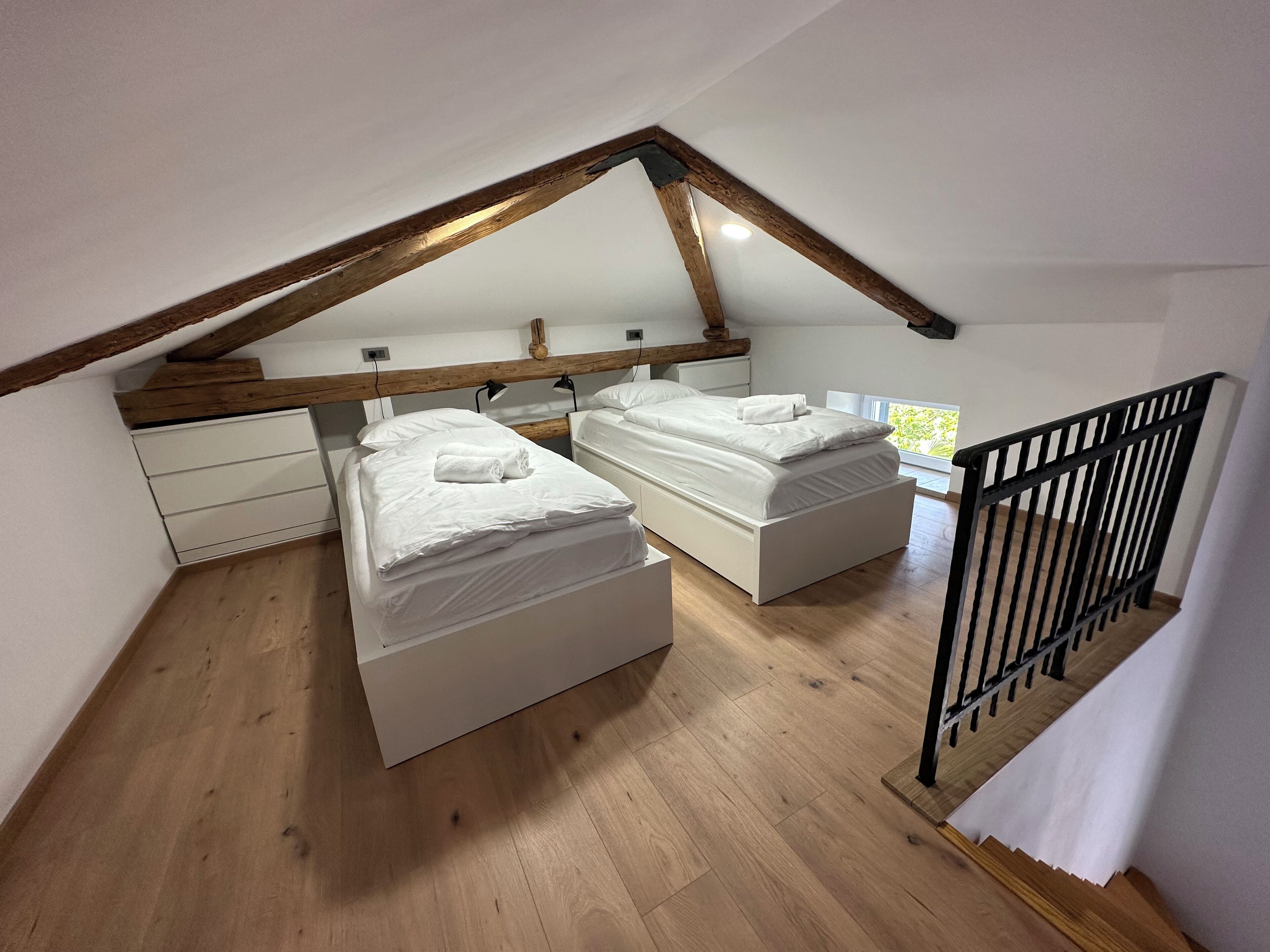 A bedroom with two beds, wooden beams, white walls, and a black railing.