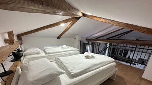 A bedroom with two beds, wooden beams, a black desk, and a window overlooking a balcony. - Apartment Olivia (Piran)