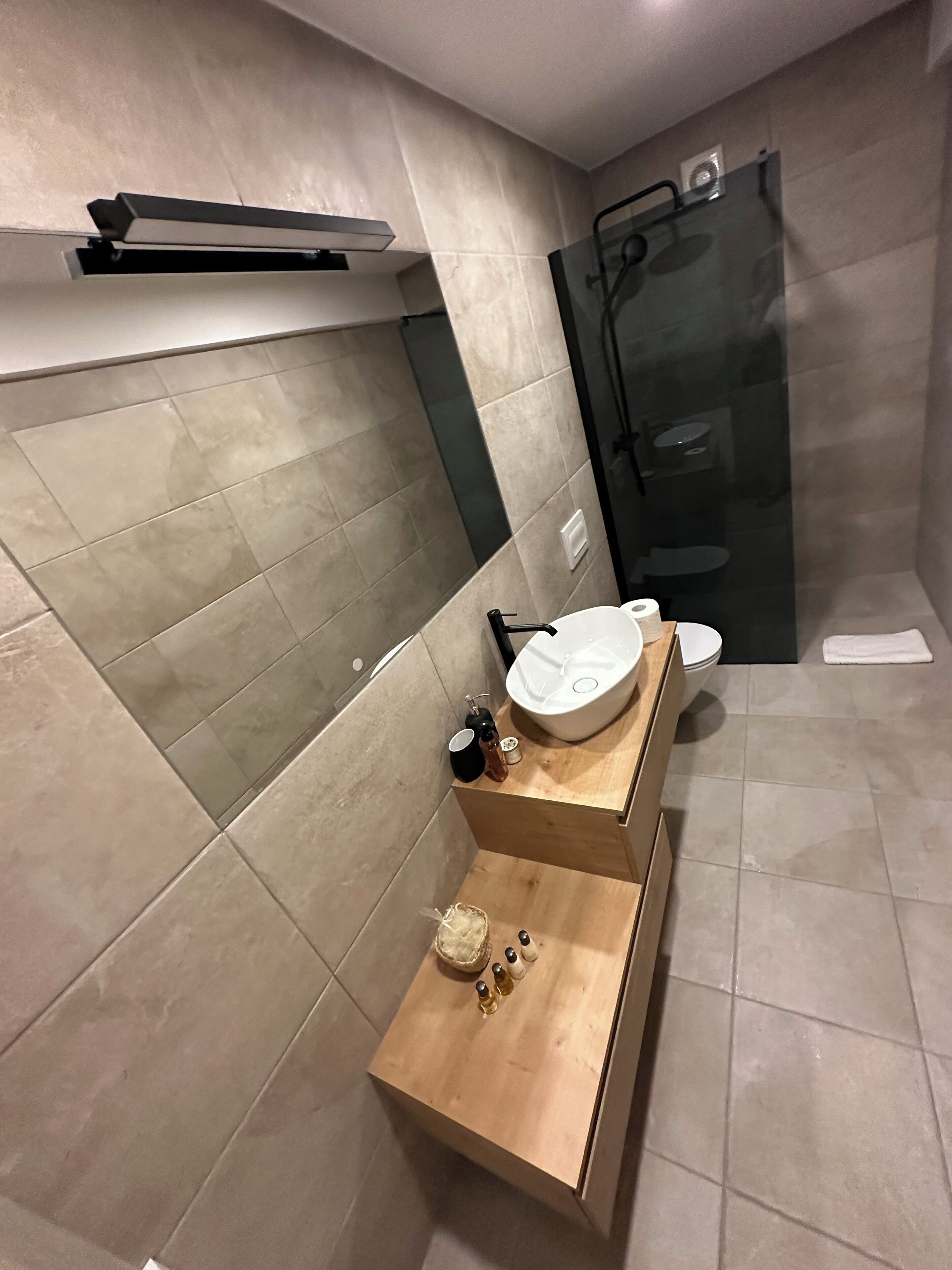 A modern bathroom with a wooden vanity, a large sink, and a glass shower enclosure.