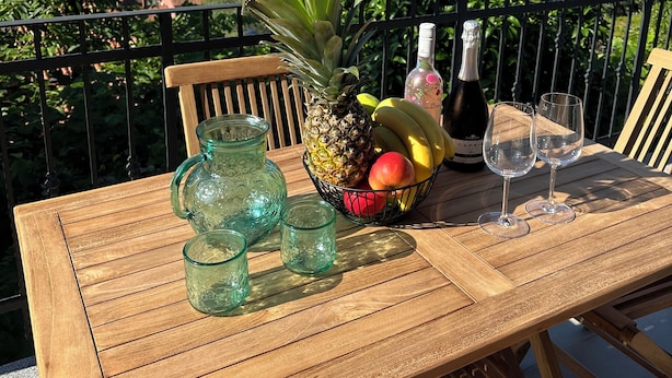 A wooden table with a fruit bowl, glasses, and a bottle on a balcony overlooking a scenic view. - Apartment Olivia (Piran)