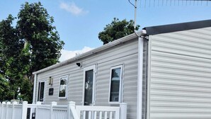 Une maison mobile à l’extérieur blanc, avec une cour avant clôturée et une antenne parabolique sur le toit.