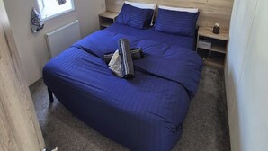 Une chambre à coucher avec un grand lit, une fenêtre avec des rideaux, une tête de lit en bois et une table de chevet avec une lampe.